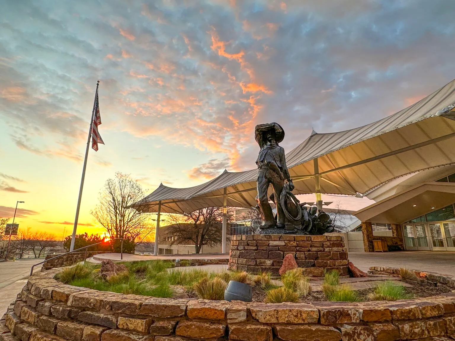 Cowboy statue near modern building at sunset